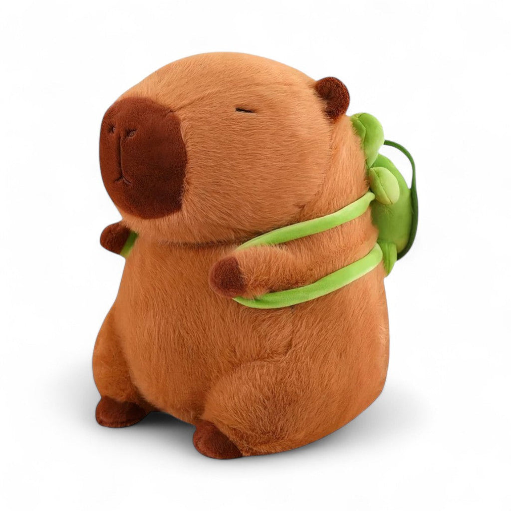 Peluche capybara marrone con zaino tartaruga verde, seduto su sfondo bianco.