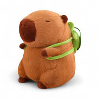 Peluche capybara marrone con zaino tartaruga verde, seduto su sfondo bianco.