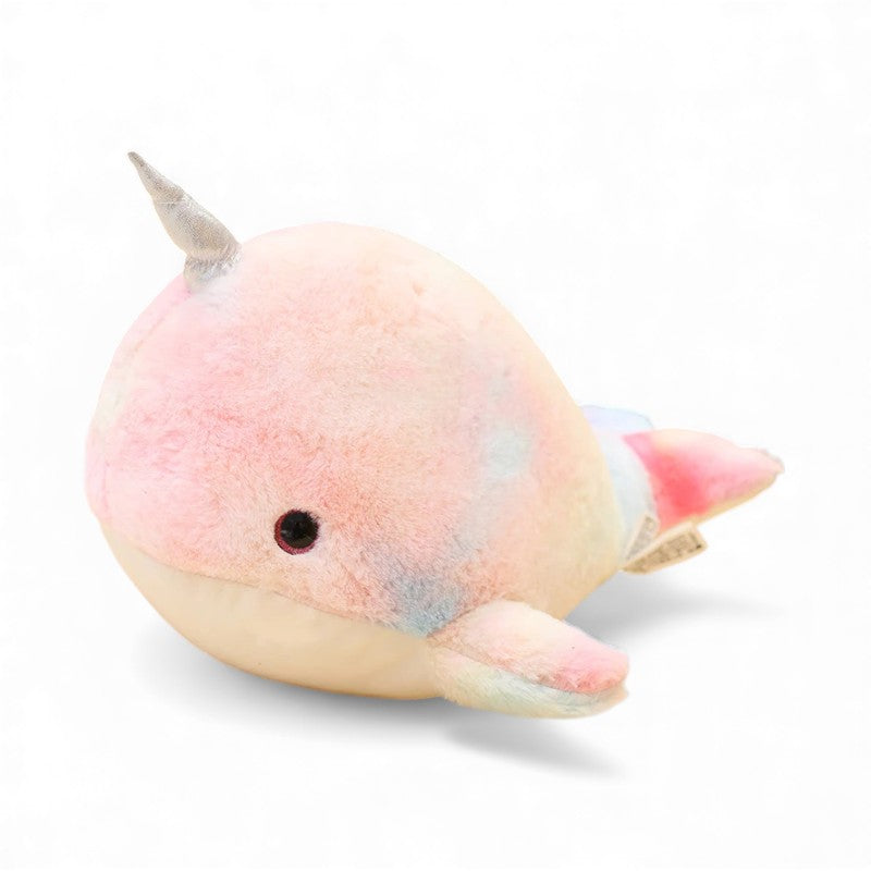 Peluche narvalo tondo e morbido, dai colori pastello rosa, blu e giallo, con un piccolo corno argentato sulla testa e due pinne ai lati, posato su sfondo bianco.