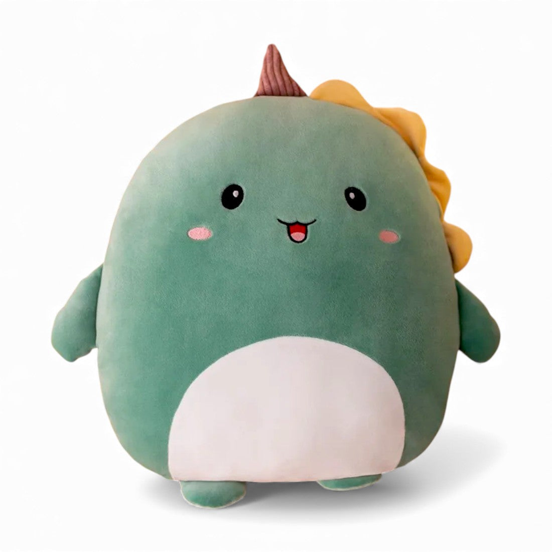Peluche dinosauro verde tutta tonda, con piccola pancia chiara, occhi neri rotondi, zampe corte e creste morbide sulla testa e sul dorso, posata da sola su sfondo bianco.