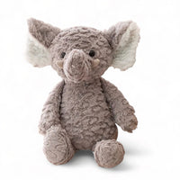 Elefante di peluche grigio, grandi orecchie bianche, occhi neri lucenti, seduto su sfondo bianco.