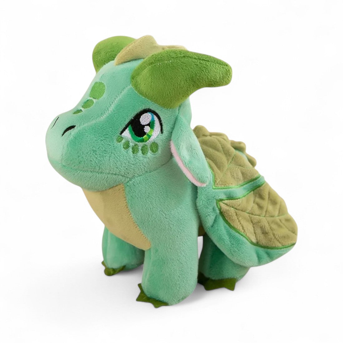 Piccolo peluche drago verde tenero con pancia chiara, grandi ali a forma di foglia, occhi espressivi, corna verdi, su sfondo bianco.