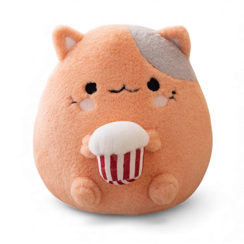 Cuscino peluche rotondo raffigurante un gatto arancione con una macchia grigia sulla testa, guance rosa, naso rosa, piccole orecchie rotonde, che tiene un cupcake rosso e bianco sulla pancia, posato su sfondo bianco