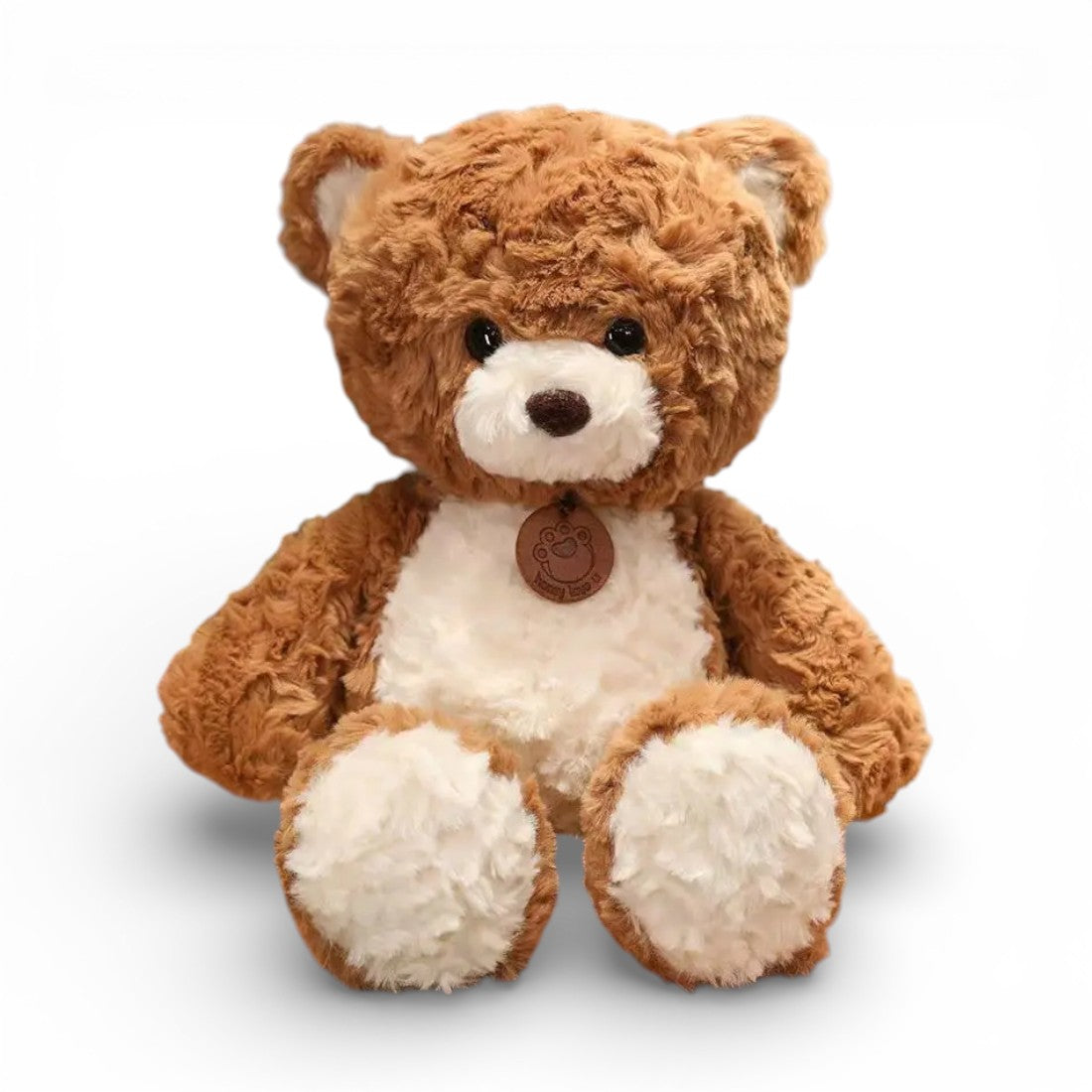 Un orso di peluche marrone chiaro soffice con pancia bianca morbida, occhi tondi neri espressivi, musetto adorabile, piccole orecchie tonde, zampe paffute e medaglione tondo in pelle intorno al collo, su sfondo bianco uniforme.