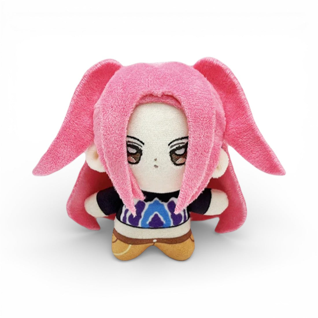 Peluche bambina con lunghi capelli rosa, con grandi occhi rossi ambrati ricamati, vestita con una maglietta nera viola e blu e un pantalone arancione, su sfondo bianco.